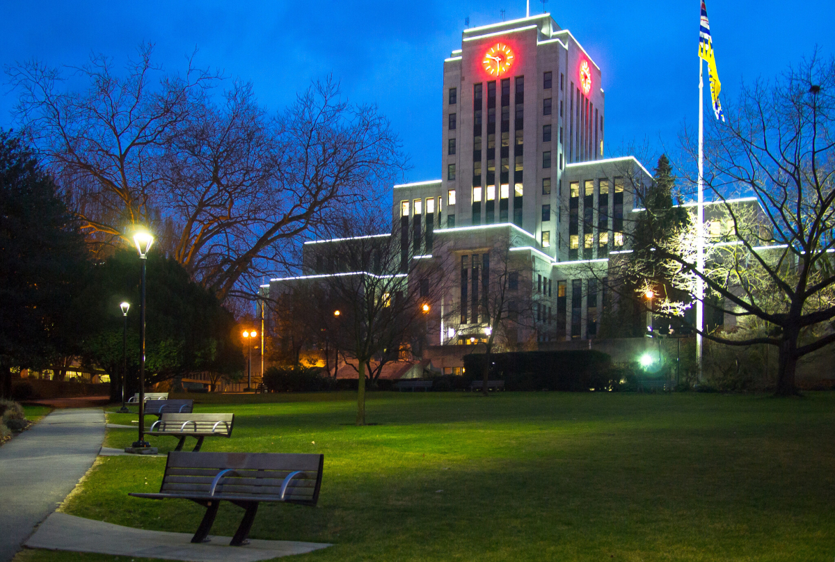 Vancouver City Hall at dusk, clock tower lit, with lawn and benches in the foreground